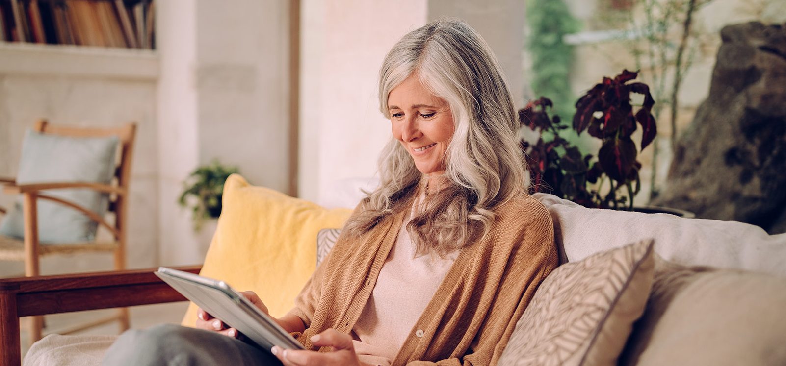 senior woman sitting on a couch smiling and looking at her tablet senior woman sitting on a couch smiling and looking at her tablet