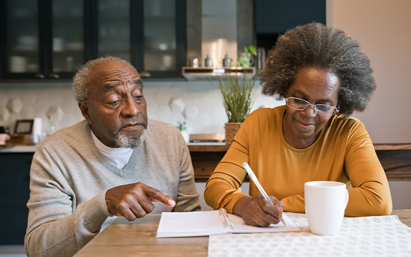 woman writing in a notebook next to her senior father with dementia