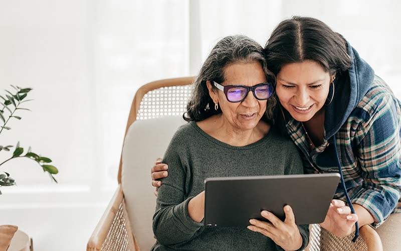 Senior woman using a tablet with her adult daughter looking over her shoulder and assisting