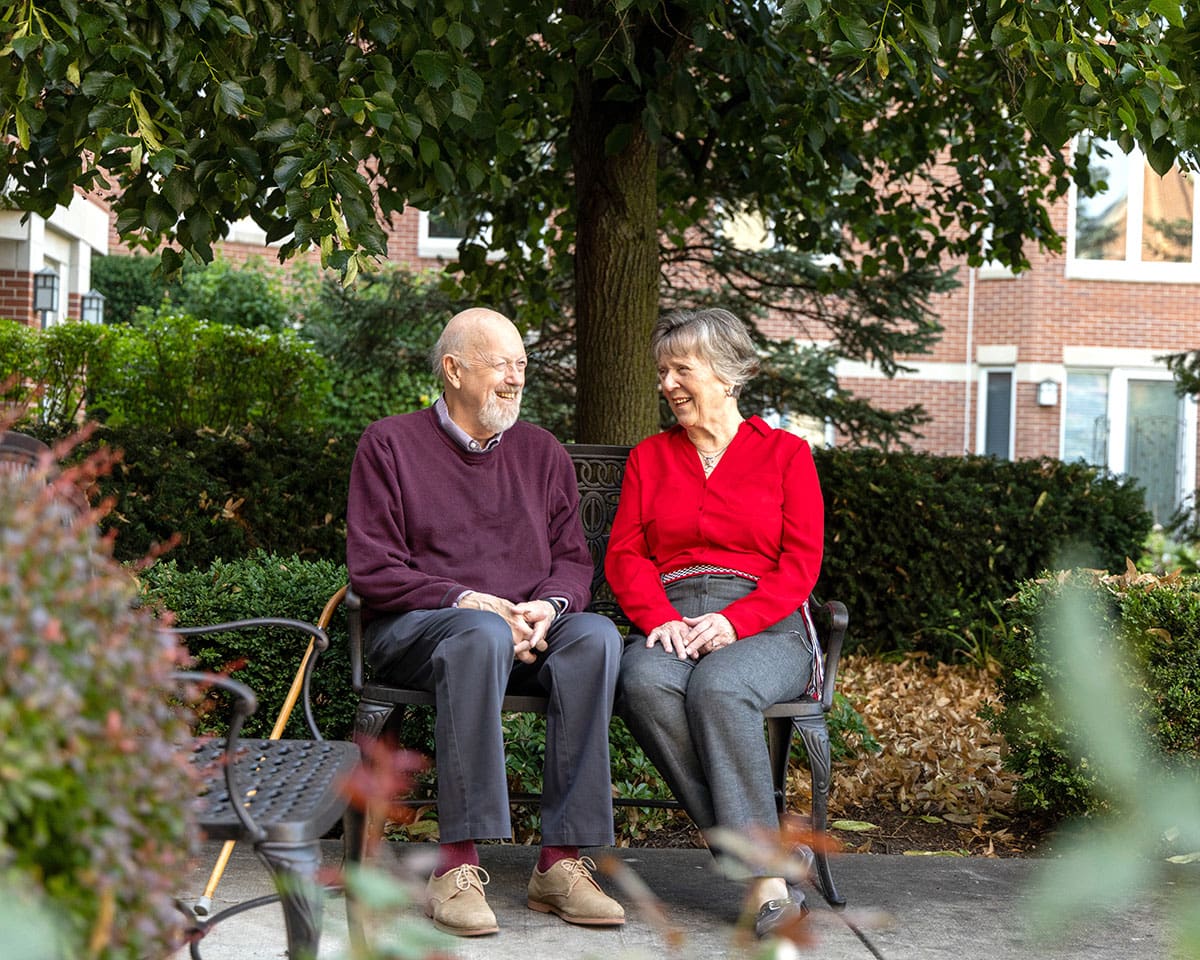 Resident couple sitting on a bench under a tree at Lake Forest Place