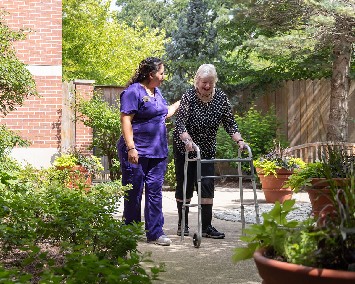 Skilled Nursing patient walking outdoors at Lake Forest Place with the assistance of her caregiver