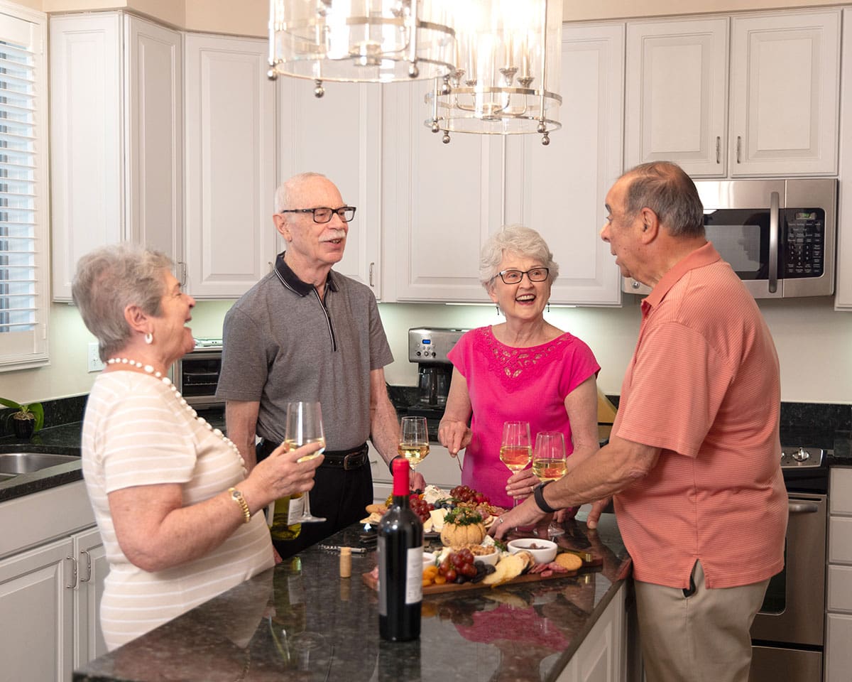 Two resident couples laughing over wine and a charcuterie plate in their apartment at Lake Forest Place