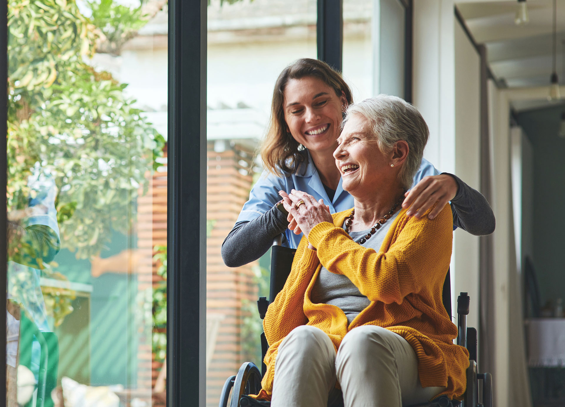 Respite Care patient sitting by a window in her wheelchair with her caregiver at Lake Forest Place