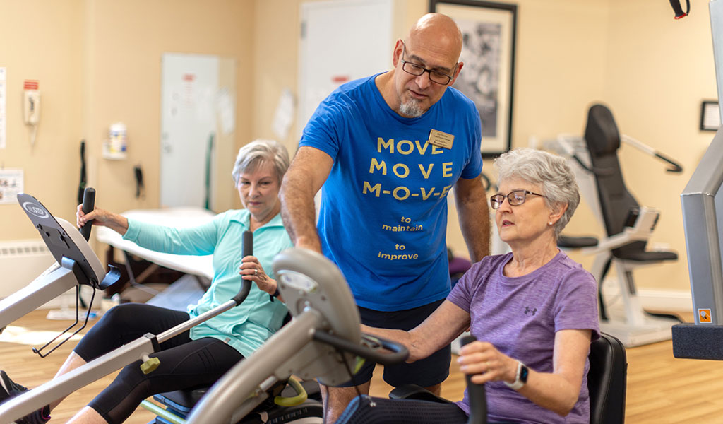 Two resident women working with a trainer in the fitness center at Lake Forest Place Two resident women working with a trainer in the fitness center at Lake Forest Place