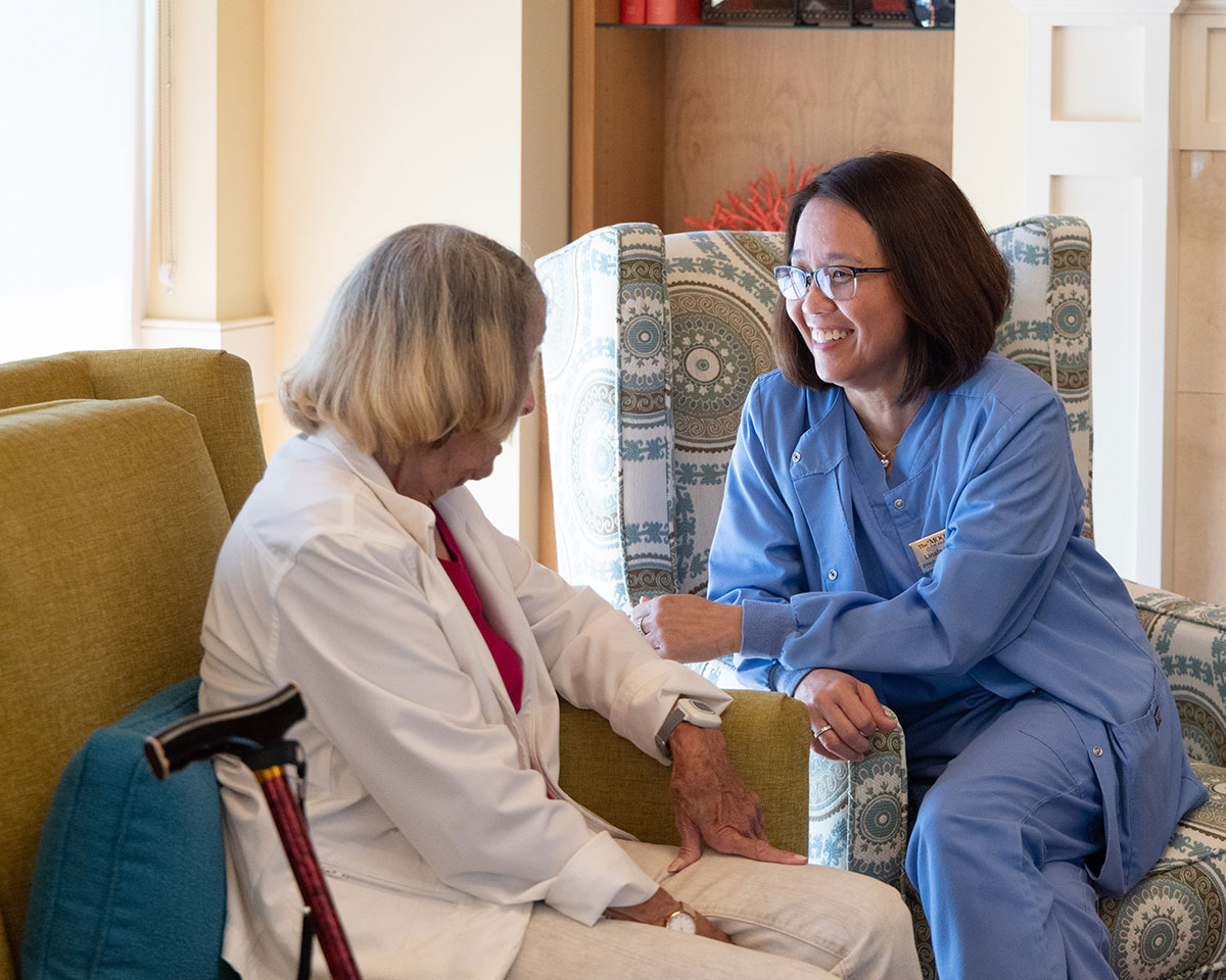 Assisted Living resident sitting on a sofa and speaking with her caregiver at The Moorings of Arlington Heights