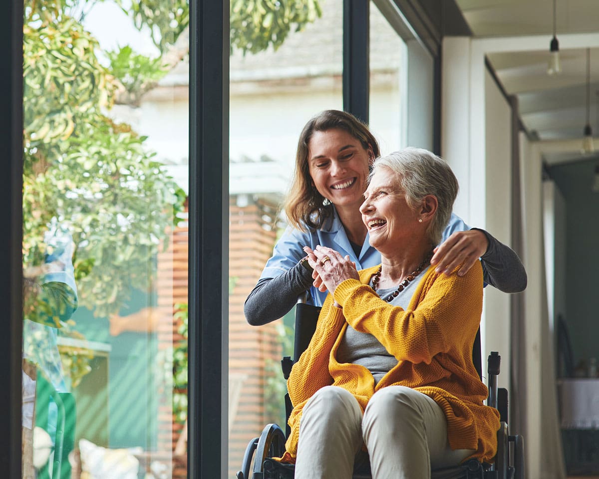Skilled Nursing patient sitting by a window in her wheelchair with her caregiver at The Moorings of Arlington Heights
