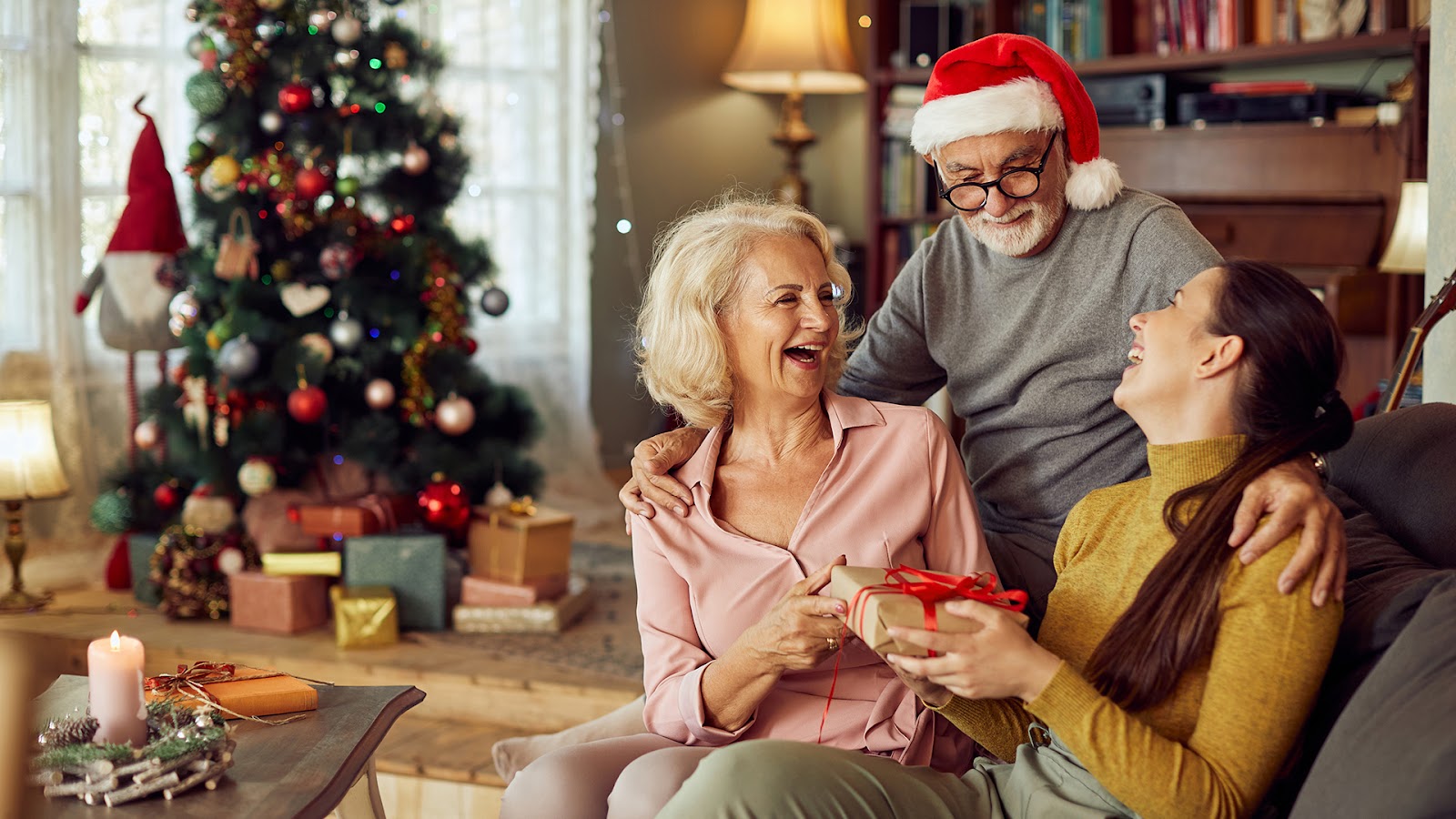 Moorings November Blog Featured Image Senior couple having fun while surprising their adult daughter with a gift on Christmas day at home.