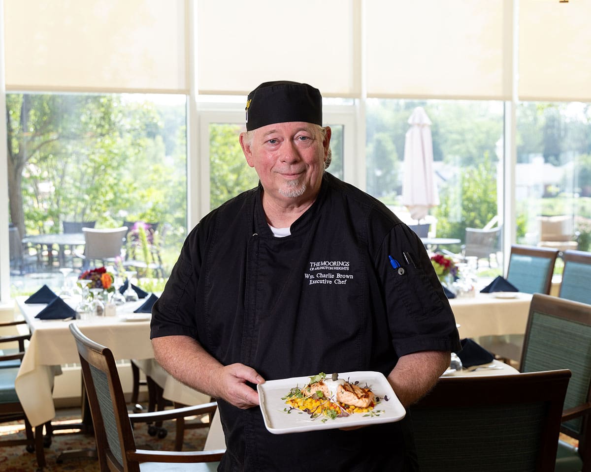 Chef at The Moorings of Arlington Heights proudly displaying a delicious plate of food he has prepared