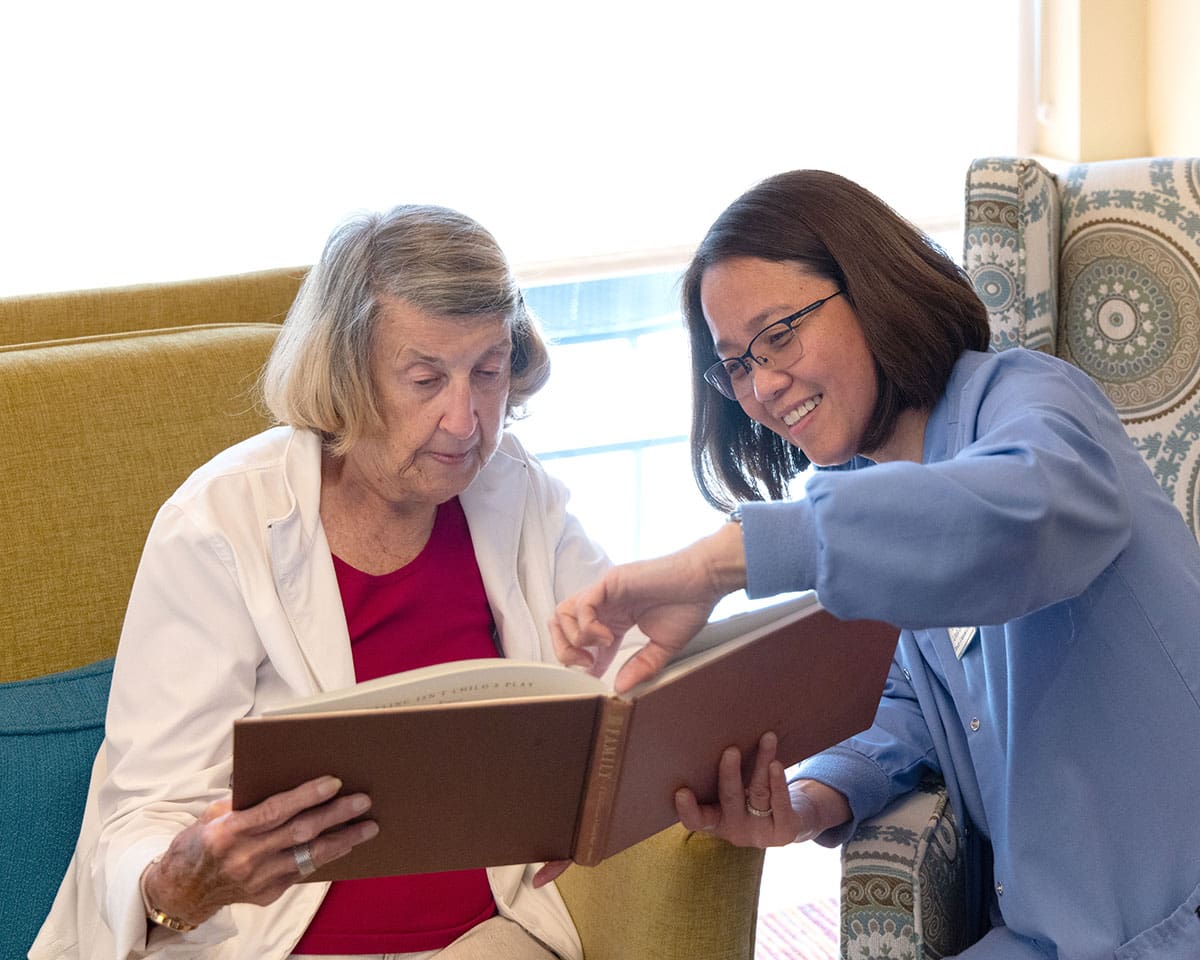 Senior woman reading a book with her caregiver at The Moorings of Arlington Heights