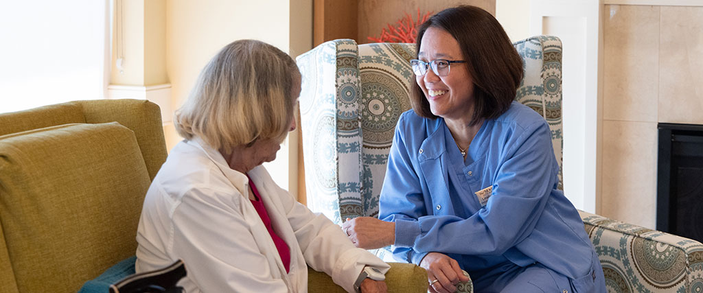 Skilled Nursing patient sitting on a sofa and speaking with her caregiver at The Moorings of Arlington Heights Skilled Nursing patient sitting on a sofa and speaking with her caregiver at The Moorings of Arlington Heights