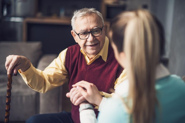 A granddaughter sitting down with her smiling grandfather and clasping his hand in hers