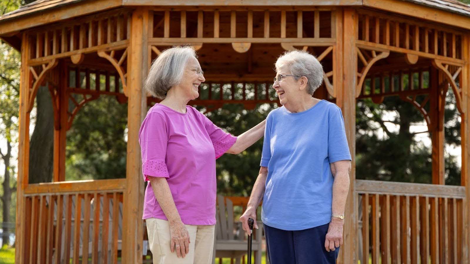 PHMA March 2024 Blog Featured Image 2 senior women talking by a gazebo at The Moorings of Arlington Heights