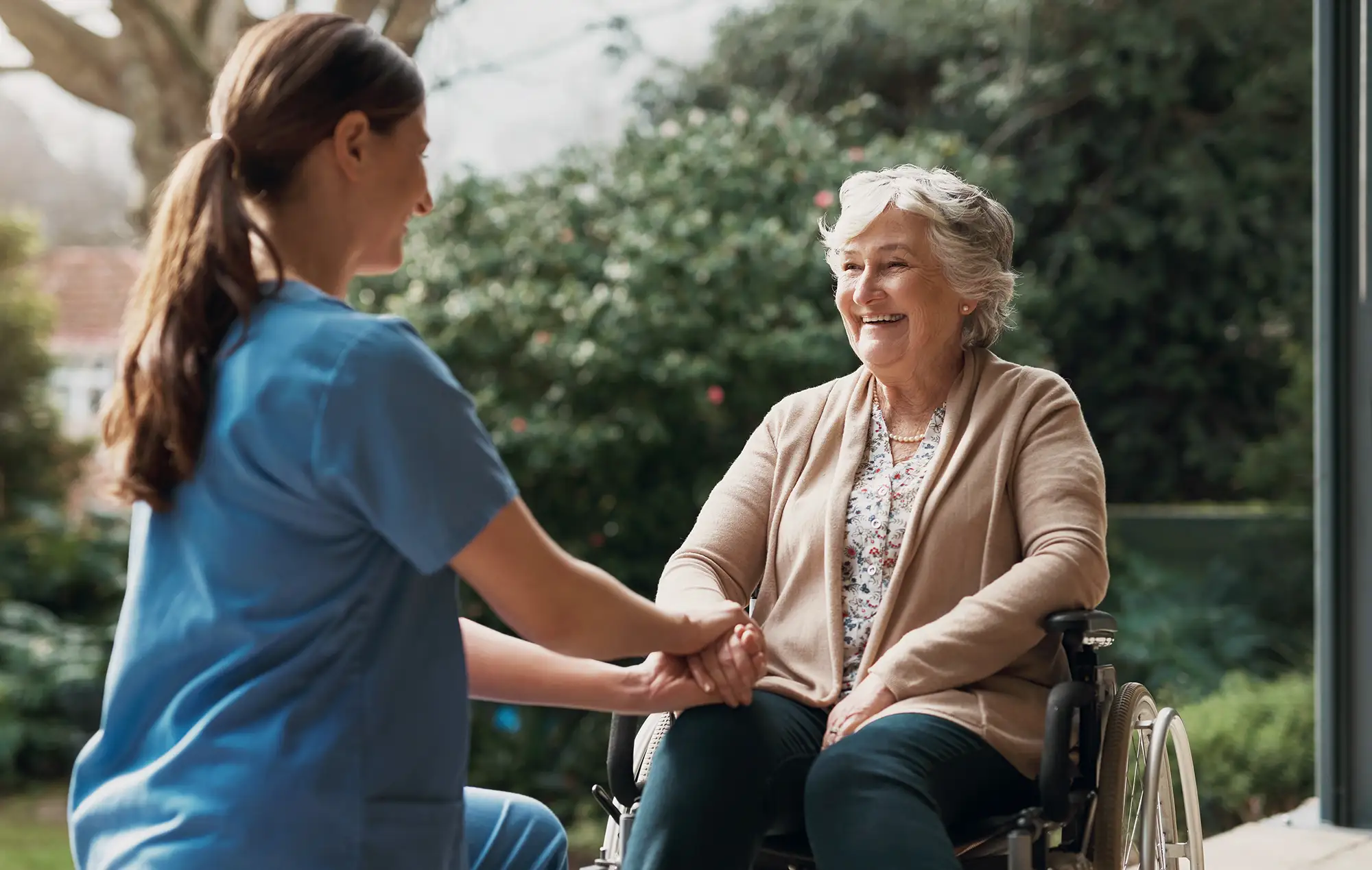Senior woman in a wheelchair holding hands with her caregiver
