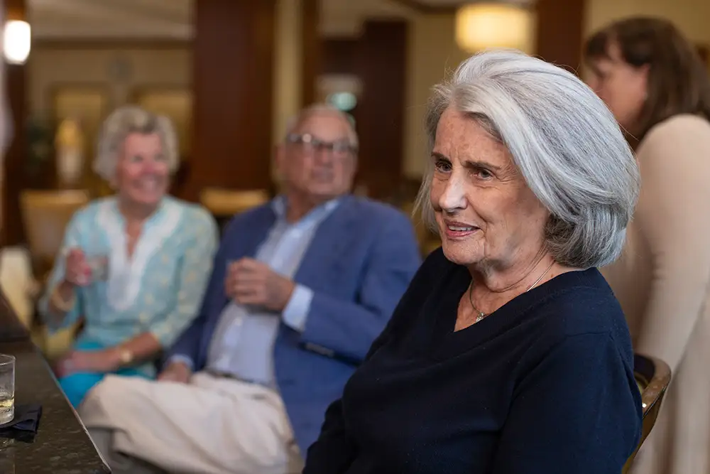 A close-up of a Lake Forest Place resident smiling during a social gathering, while other residents chat and hold drinks