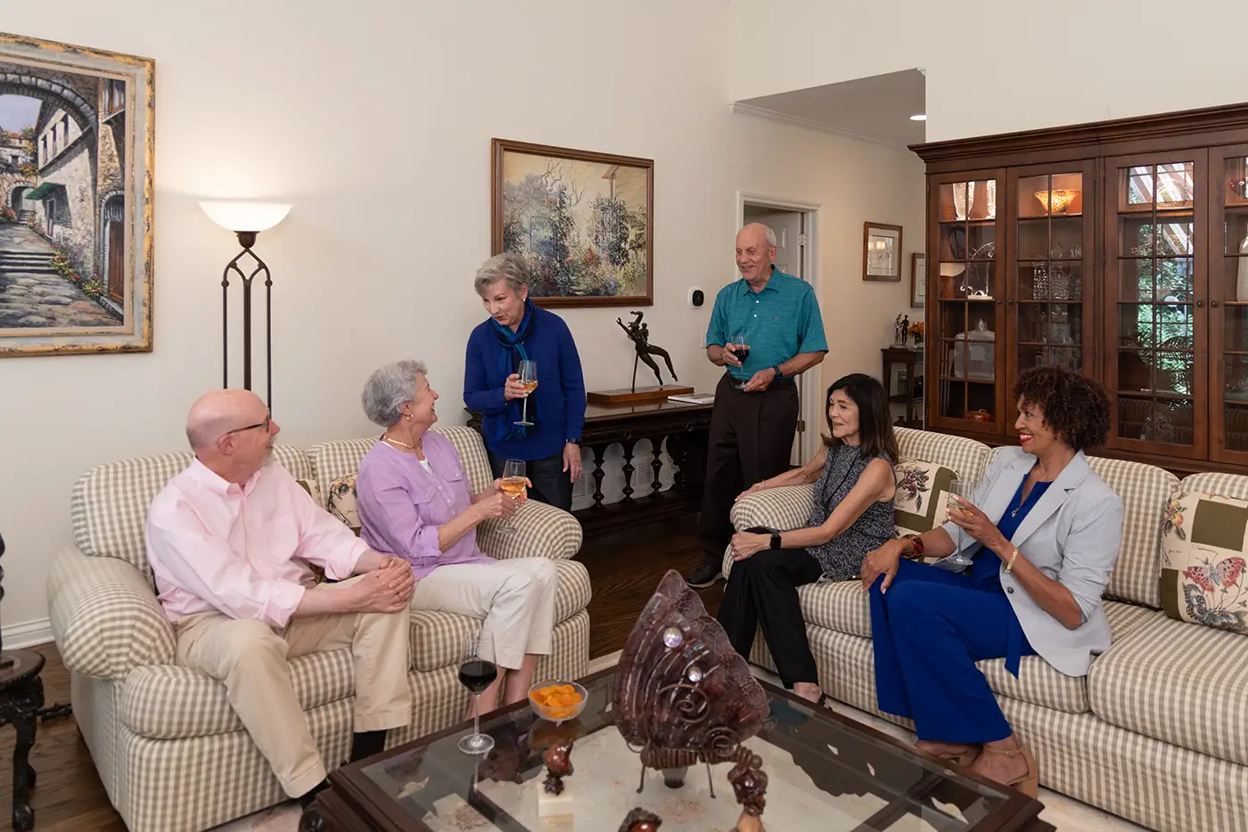 A group of Lake Forest Place residents socialize and enjoy drinks in a warm, spacious living room, highlighting the welcoming feel of cottage living.