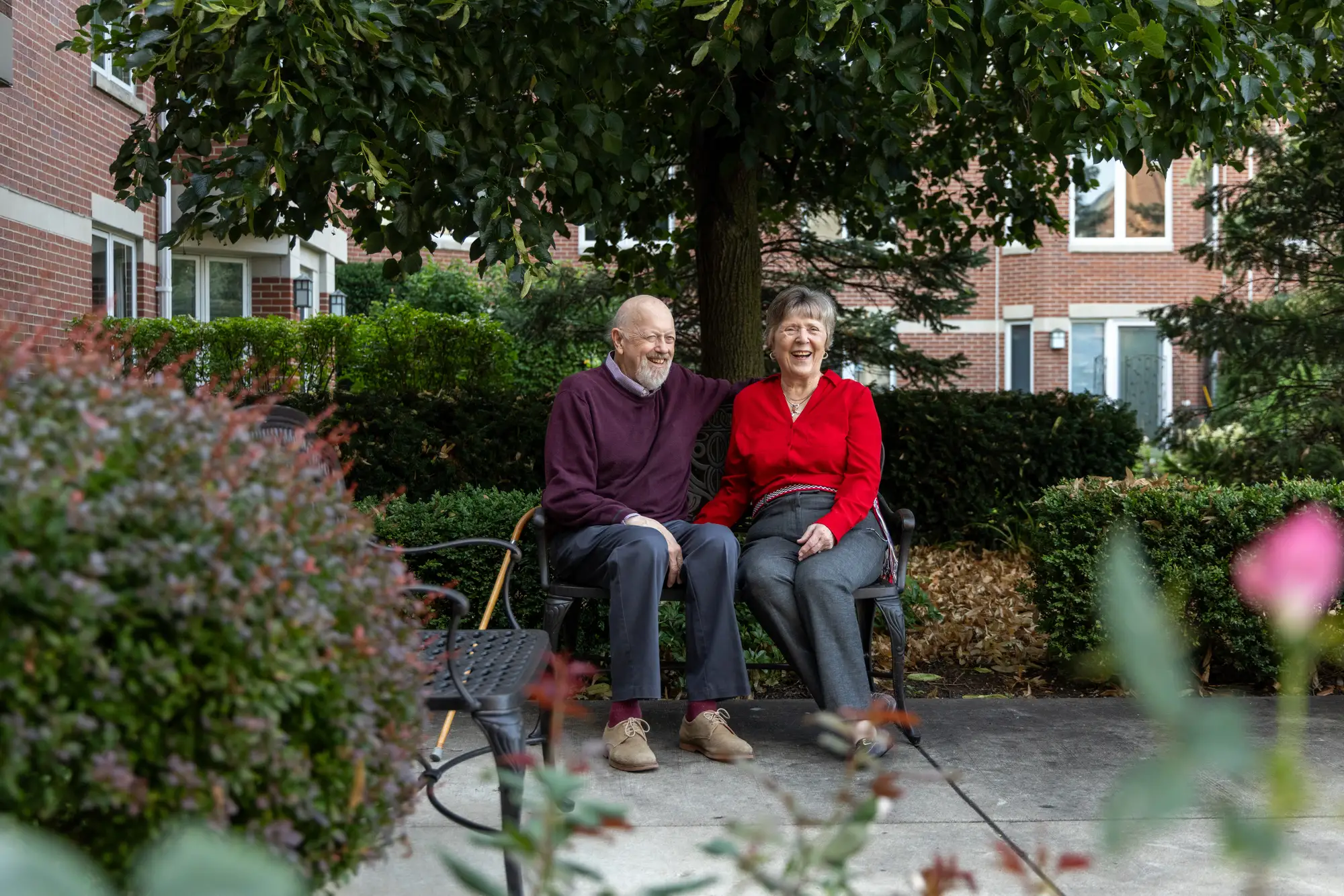 senior couple sits on a bench outside of their independent living community