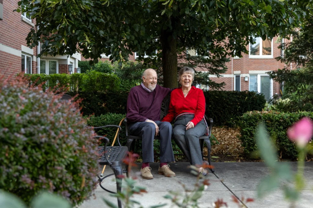 senior couple sits on a bench outside of their independent living community