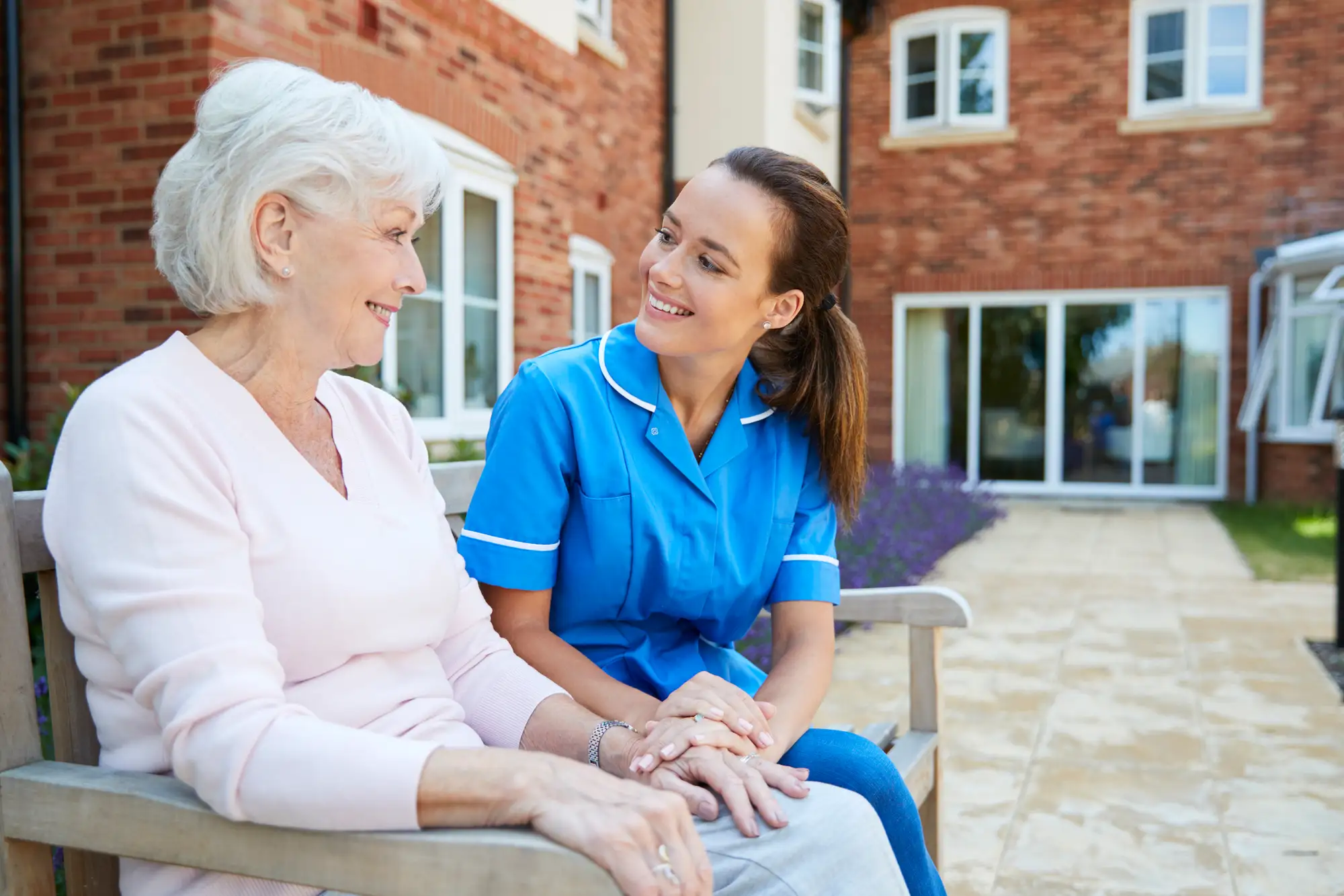 Senior Woman Sitting On Bench And Talking With Nurse In Life Plan Community