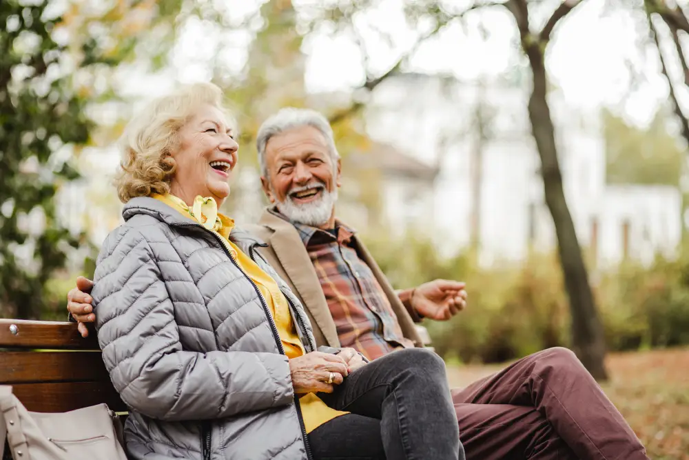 a senior couple laughing on a park bench on a fall day