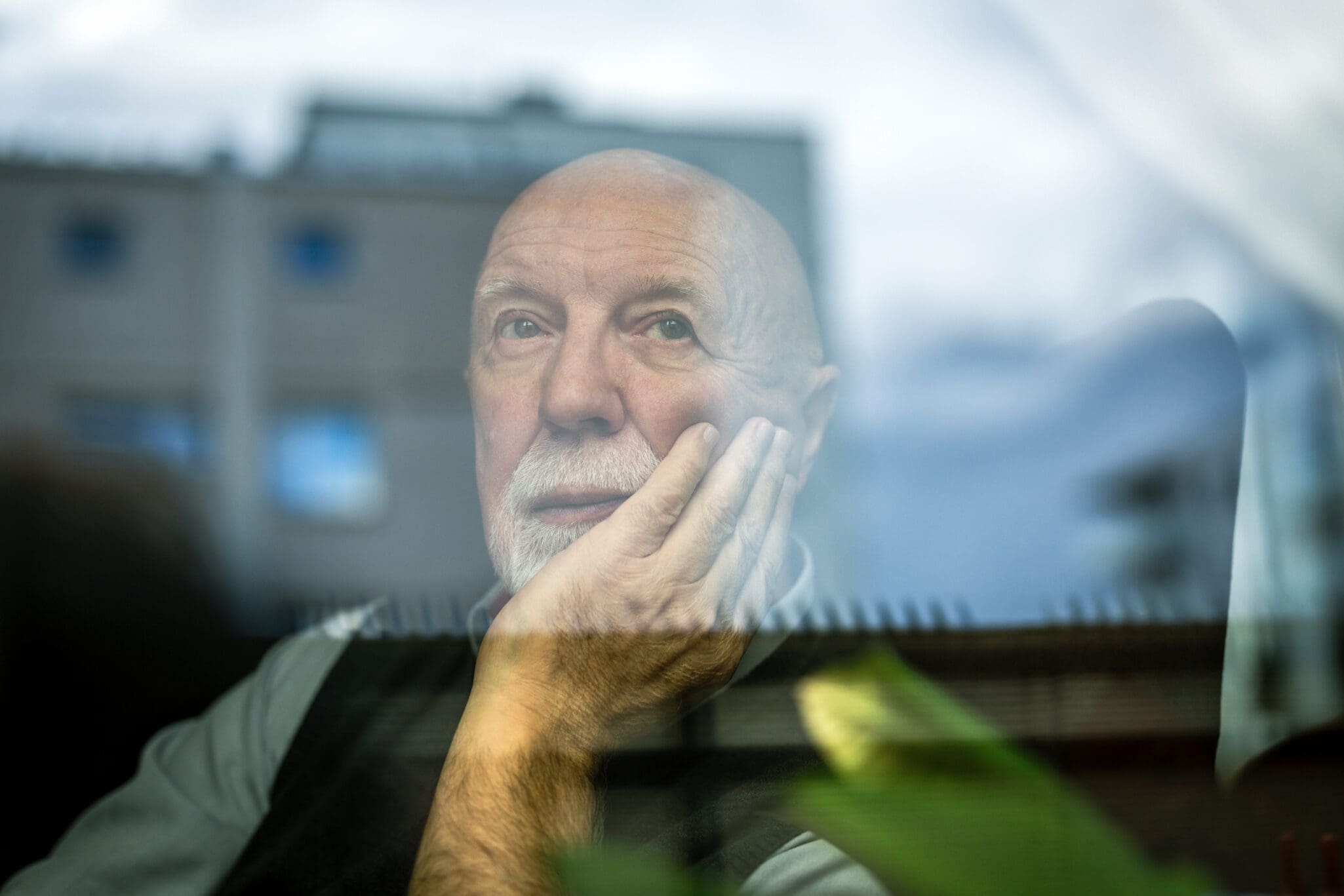 Portrait of thoughtful senior man looking through window senior man in front of window looking out