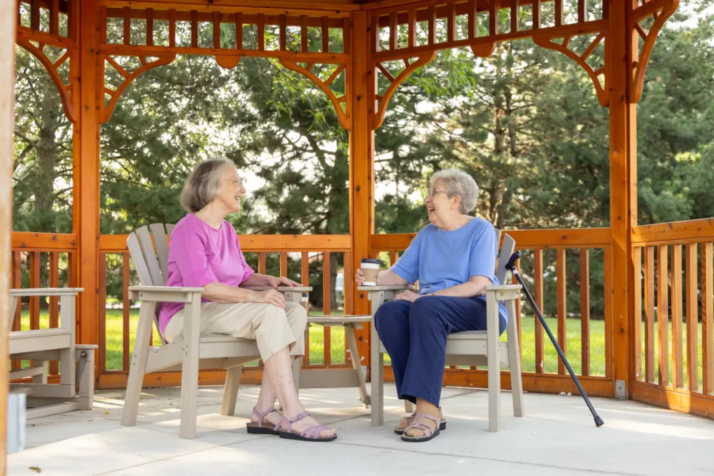 two senior women residents of The Moorings of Arlington Heights sit and chat in the community's gazebo