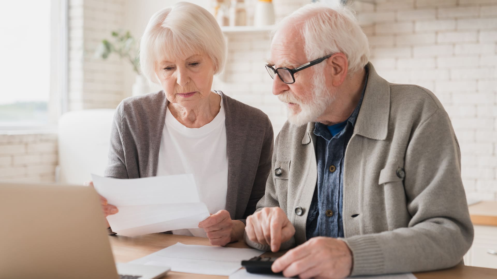 calculating expenses Senior couple counting funds on calculator, at home using laptop.