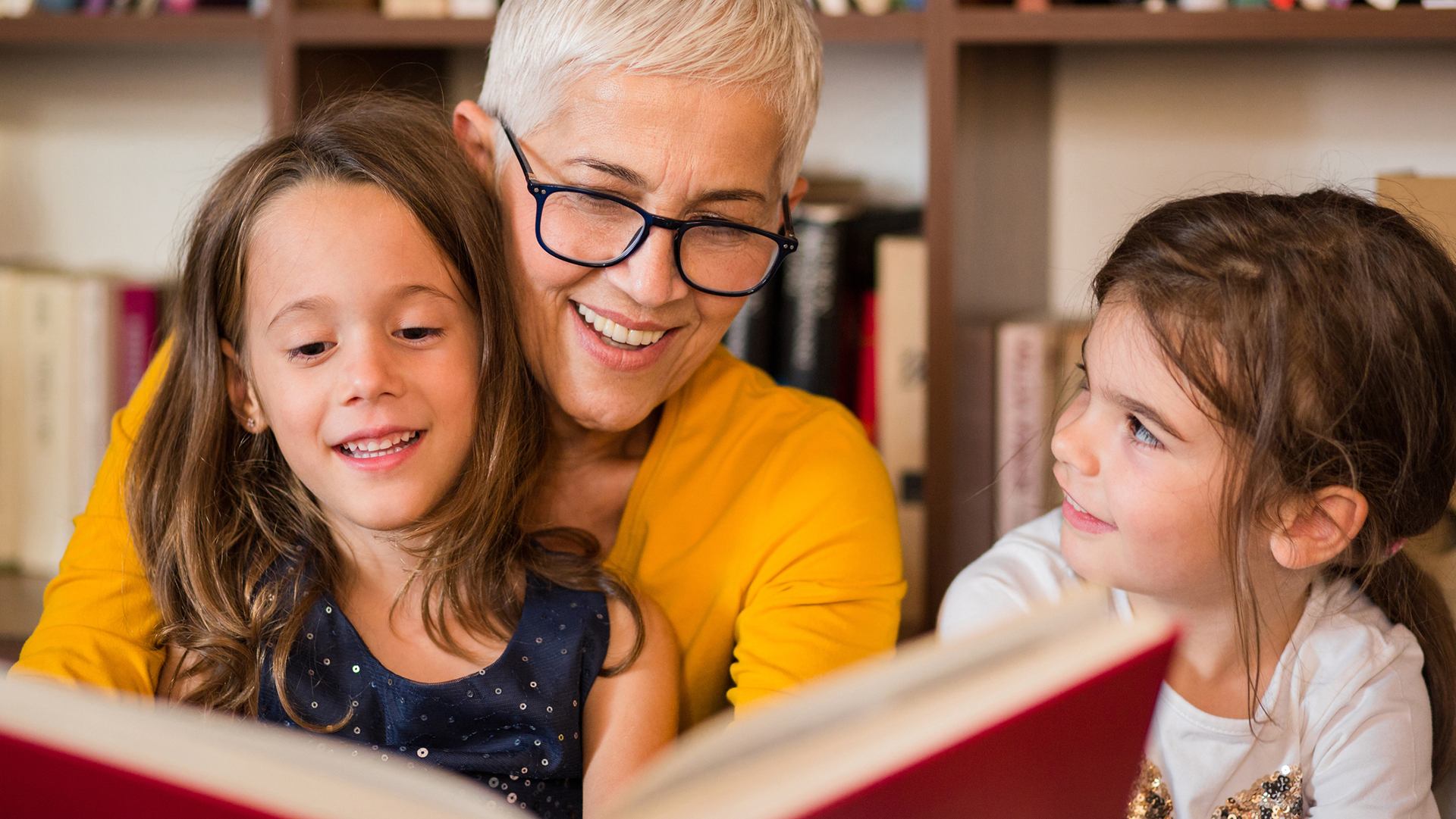 happy older woman reading tales for her two beautiful granddaughters Old woman reading to granddaughters