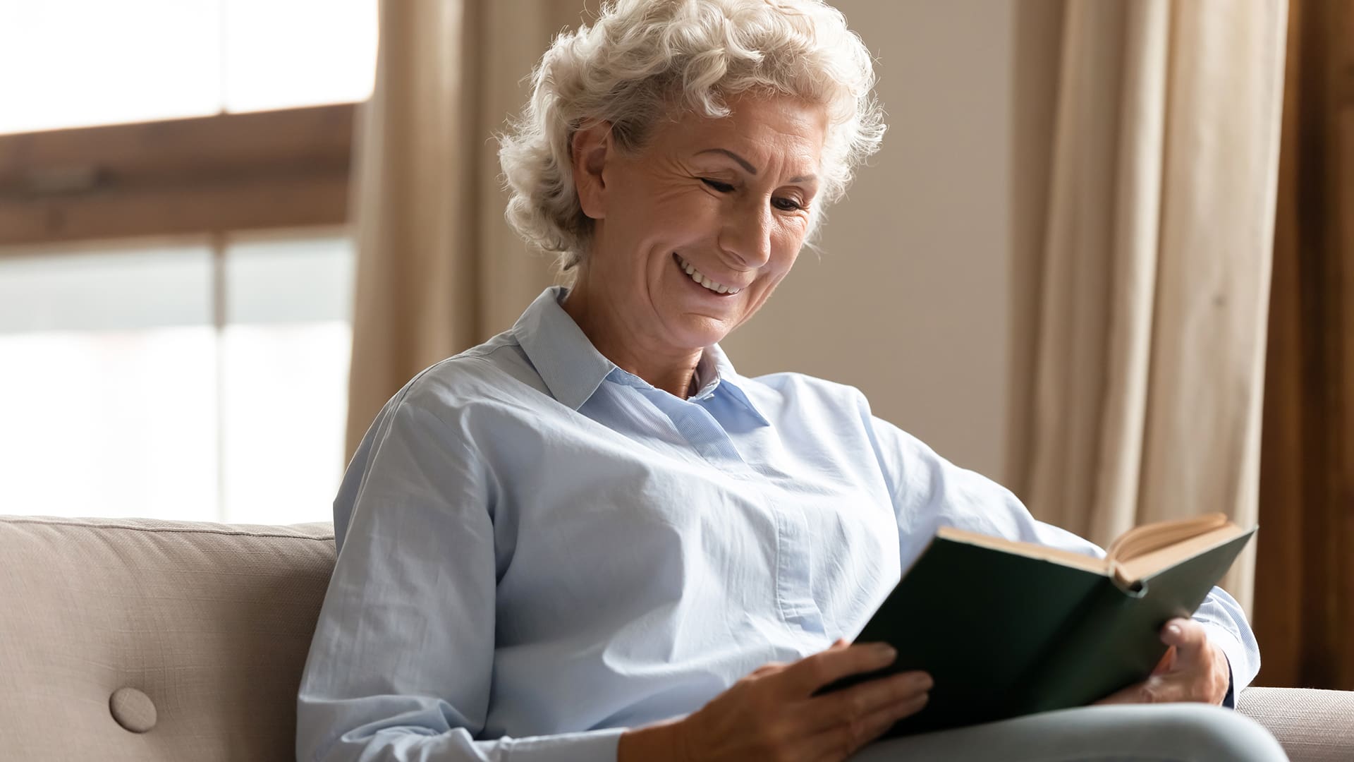 Smiling mature woman enjoy free time reading interesting book Smiling mature woman enjoy free time having good hobby pastime reading interesting literature holding book seated on comfy couch in living room at home alone