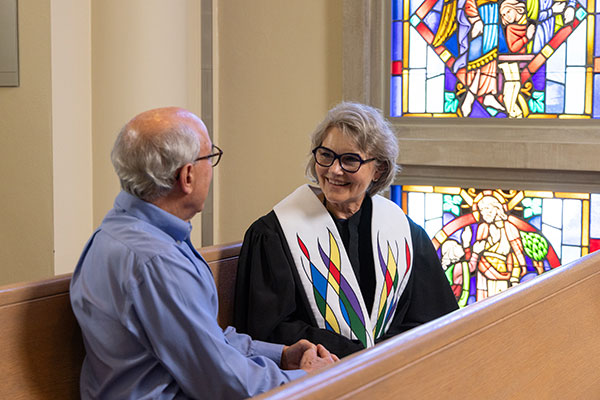Clergywoman sitting with a senior man in a pew at the chapel at Westminster Place
