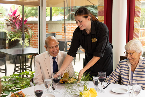 Server delivering food to a senior couple dining at Westminster Place