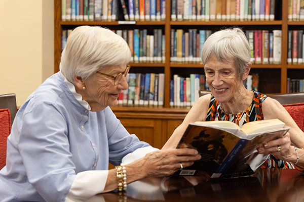Two senior women reading in the library at Westminster Place
